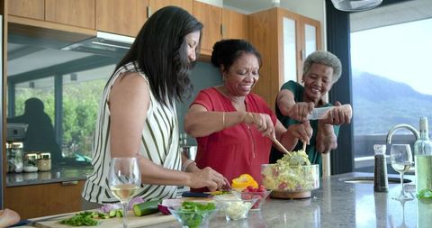 African american women cooking together in sunlit kitchen stirring fresh salad
