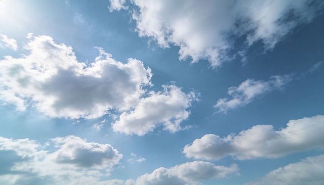 Drifting Cumulus Clouds Filling Expansive Blue Sky with Soft Sun Glare and Horizon
