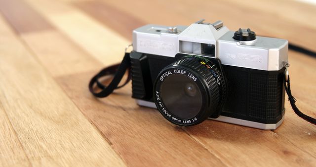 A vintage camera rests on a wooden surface, capturing a sense of nostalgia for traditional photography. Its classic design and optical color lens suggest a bygone era of film-based image capturing.