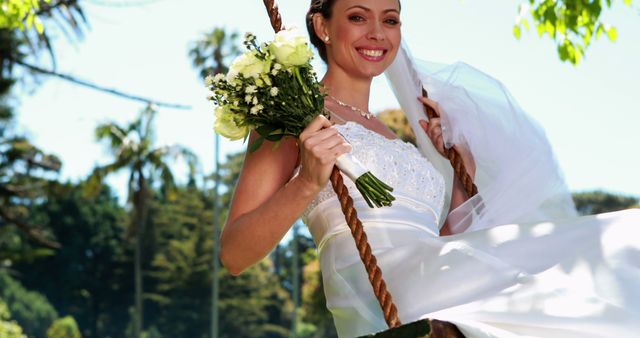 Pretty bride sitting on a swing smiling at camera on her wedding day
