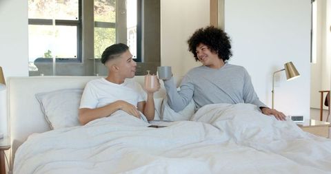 Two friends enjoying morning coffee in bed relaxed at modern home