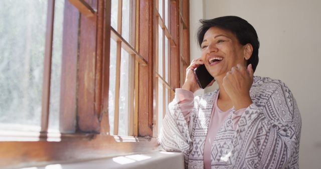 African american senior woman smiling while talking on smartphone near the window at home. retirement lifestyle living concept