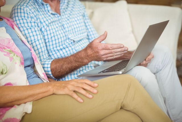 Mid section of senior couple using laptop in living room at home
