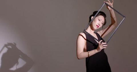 Elegant asian woman posing with frame against minimalist background