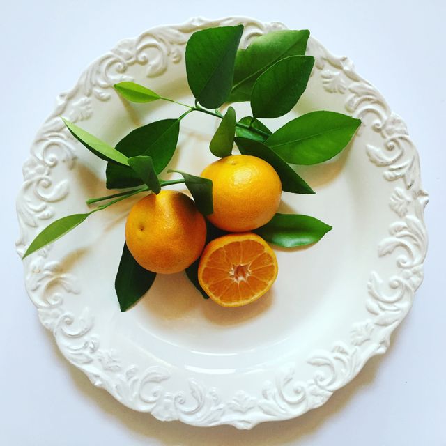 Shows fresh oranges with vibrant green leaves on ornate white plate, evoking a sense of freshness. Suitable for promoting organic lifestyle, culinary content, or kitchen decorations. Perfect for health foods, kitchenware marketing, or seasonal fruit promotions.