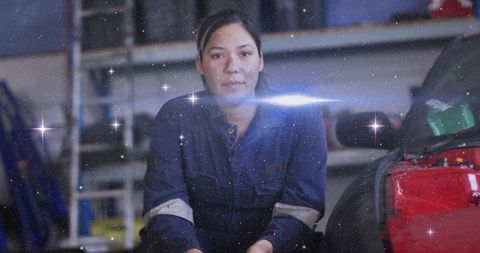 Female auto technician sitting in garage wearing blue coveralls with reflective cuffs