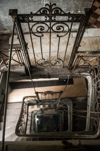 Detailed view of an aged spiral staircase with a vintage metal handrail in an old building. Perfect for use in projects emphasizing historical architecture, urban decay, vintage settings, or interior designs with a rustic theme.