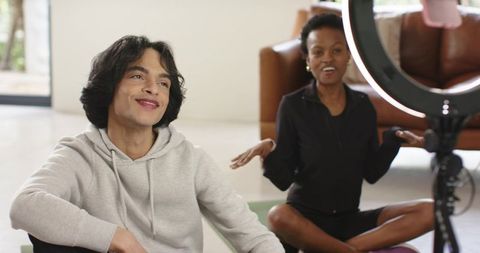 Diverse friends filming wellness and yoga content on living room mats with ring light