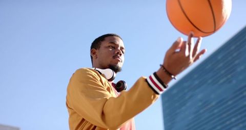 African american man spinning basketball on fingertip wearing yellow jacket and headset