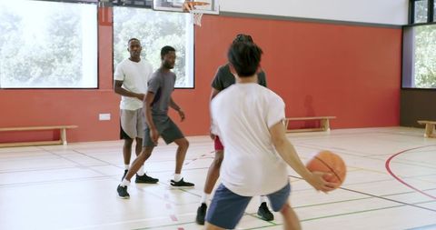 Multiracial men dribbling, driving baseline and faking moves on indoor basketball court