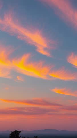 Vertical video of pink orange wispy clouds drifting over rural dusk sky with silhouette