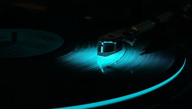 Tracking turntable tonearm tracing vinyl grooves with cyan rim glow macro reflection