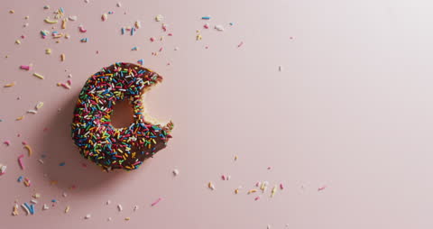 Partial Chocolate Donut with Sprinkles on Pastel Surface