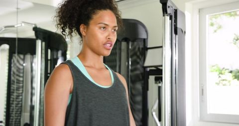 African american woman pausing during strength training at cable machine in bright gym