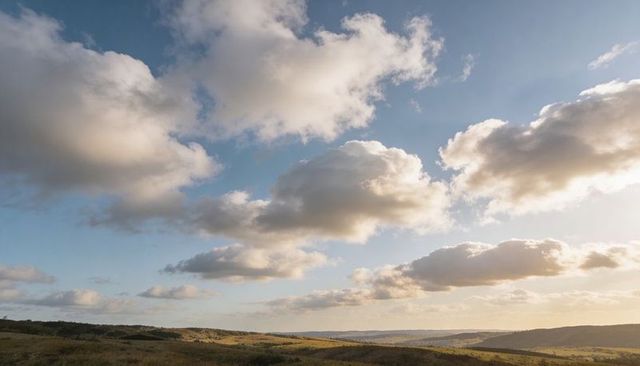 Sunlit cumulus clouds drifting over rolling pastoral hills at golden hour, expansive view