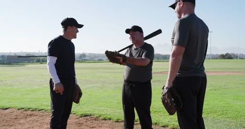 Senior Men Coaching and Practicing Baseball Batting Technique on Sunny Grass Field