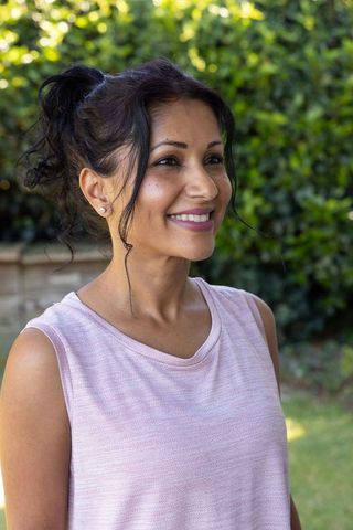 Smiling indian woman wearing pink knit top outdoors relaxed casual backyard portrait