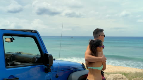 Couple Embracing by Ocean with Blue SUV in Foreground