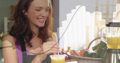 Smiling woman pouring green smoothie at kitchen counter with blender and fresh produce