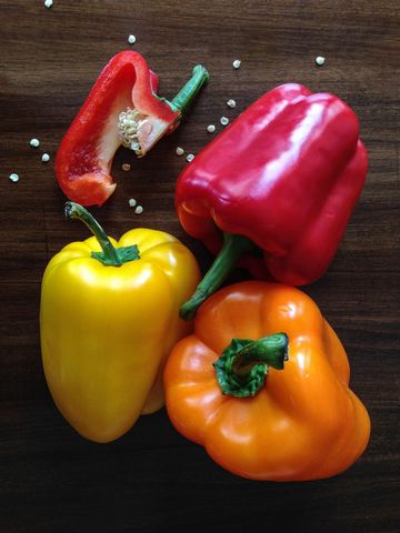 Vibrant bell peppers arranged on dark wood showing red, yellow, orange trio with seeds