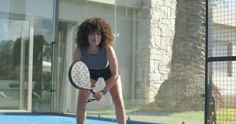 African american woman preparing to return serve on padel court wearing fitness watch
