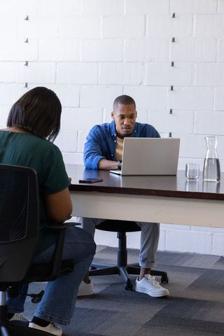 African american coworkers collaborating at minimalist office table with laptop and water
