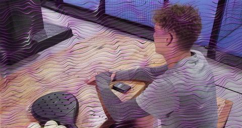 Leaning young man tapping smartphone on bed with cushions and window light, cozy morning
