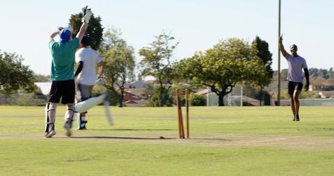 Wicketkeeper catching ball, fielder appealing run-out on park pitch