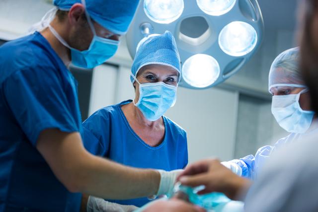 Surgeon looking at camera while colleague performing operation in operation room at the hospital