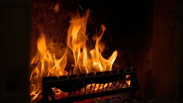 Dancing fireplace flames around metal grate casting warm glow and scattering sparks