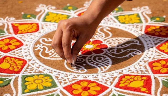 Hand creating colorful rangoli mandala on courtyard ground using white powder and pigments