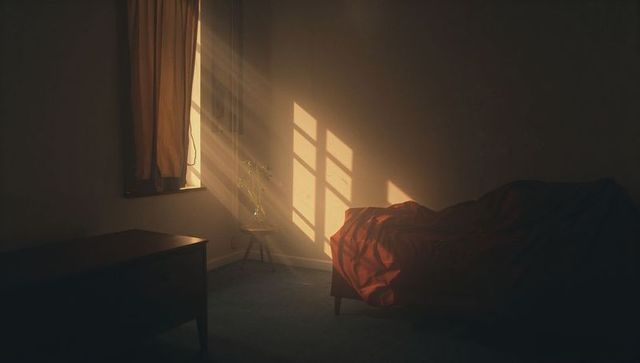 Golden-hour bedroom scene with single daybed draped in deep-red blanket and mullioned window beams