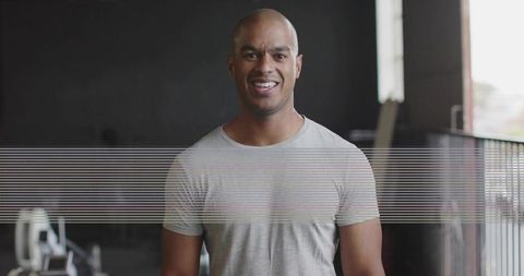 Smiling athletic man standing in gym wearing gray t-shirt natural light modern wellness