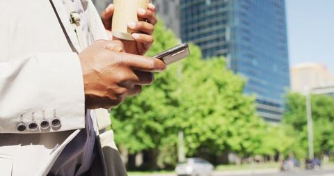 Close-up of Businessman Holding Coffee and Using Smartphone in Urban Setting