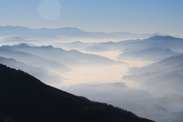 A breathtaking view of a mountain range emerging above a sea of clouds in the morning light. The mist and fog add a tranquil and peaceful atmosphere to the early morning landscape. Ideal for travel blogs, nature calendars, or background images for wellness and meditation contexts.