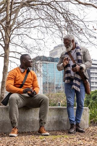 African american men chatting in urban park, casual friendship and smartphone conversation