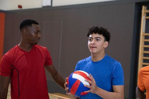 Coaching teen volleyball: diverse teammates holding red blue ball in indoor gym, teamwork