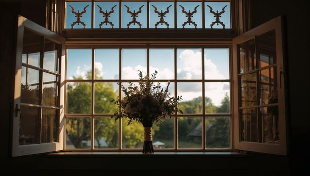 Sunlit bridal bouquet resting on wooden windowsill with open pane window and garden view