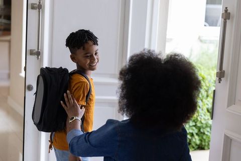 African american mother saying goodbye to son at front door with backpack and warm smile
