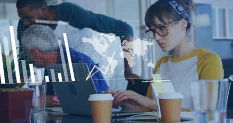 Young woman analyzing global data on laptop while team collaborates in office workspace