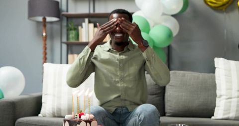 Man covering eyes while smiling during surprise birthday celebration at home with cake