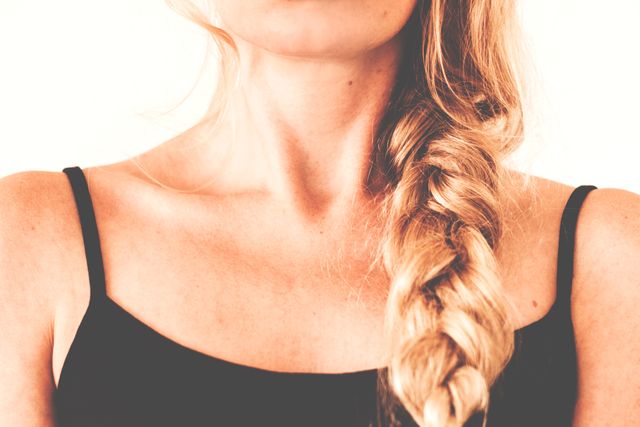 This image shows a close-up of a woman's neck and shoulders, focusing on her blonde braided hair and black strappy top. Could be used for fashion, beauty, or hair care promotions.