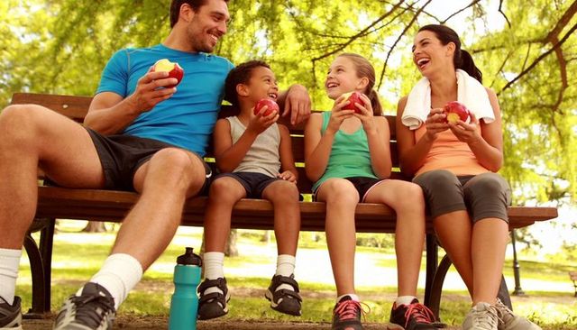 Active family relaxing and eating apples on park bench, outdoor fitness and healthy lifestyle