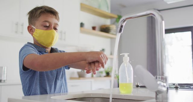 Young boy wearing a mask washing hands at kitchen sink emphasizing good hygiene practices during pandemic. Useful for topics related to health, safety, preventive measures, and hygiene especially during the COVID-19 pandemic. Can be used in educational materials, health safety guidelines, public awareness campaigns, and parenting blogs.