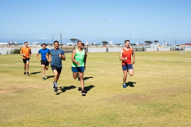 Group of multi ethnic male athletes running on a grassy field, engaging in a competitive training session. Ideal for use in articles or advertisements related to sports, fitness, teamwork, and healthy lifestyles. Perfect for illustrating concepts of athleticism, outdoor activities, and group training.