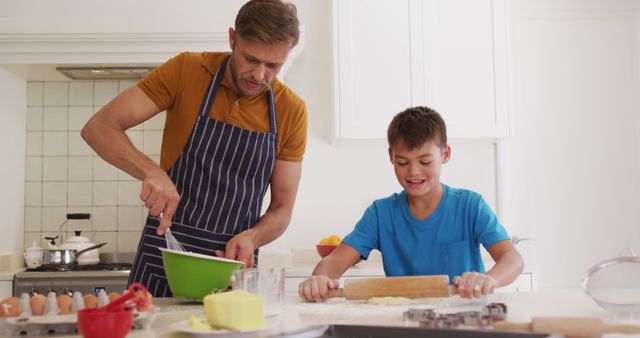 Caucasian father and son are seen actively baking together in their home kitchen. Both are smiling, enjoying quality time while teaching and learning from each other. There are baking tools and ingredients spread across the kitchen counter. This image represents family bonding, the joy of cooking together, and shared learning experiences. It can be used in family-centered advertisements, parenting blogs, cookbooks, and lifestyle magazines celebrating family values and domestic life.