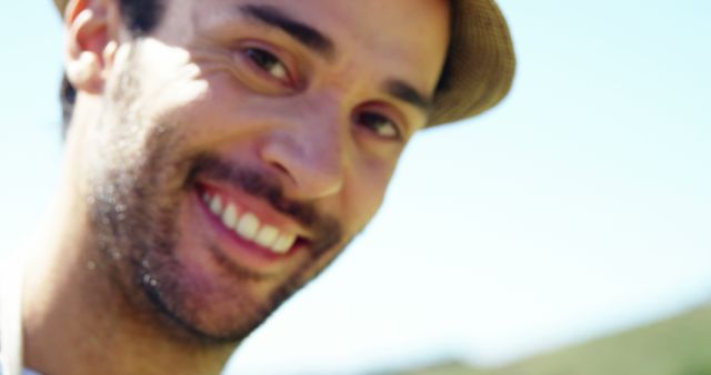 Perfect for depicting happiness, leisure activities, outdoor enjoyment, and positive moods in promotional materials, advertisements, and personal blog posts. This image showcases a close-up of a smiling man wearing a hat, enjoying sun and nature.