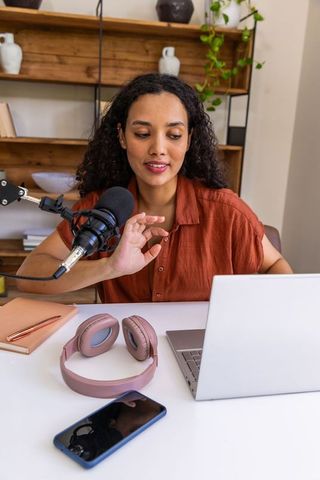 African american woman podcasting at home with microphone, laptop and headphones