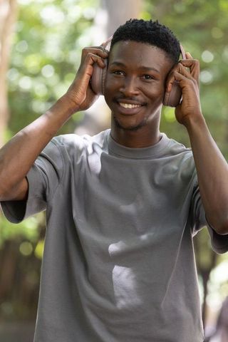Smiling african man listening to headphones in sunlit park, outdoor lifestyle portrait