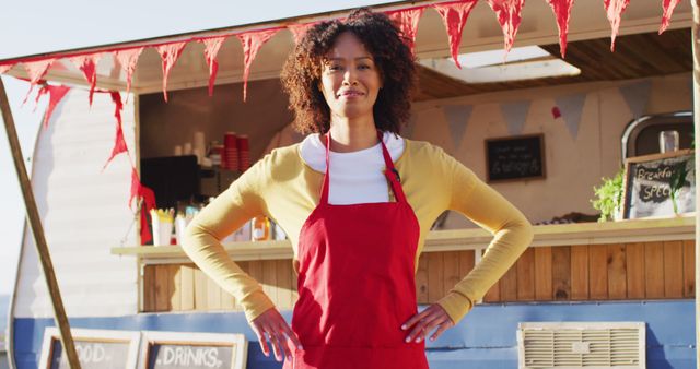 Woman with curly hair standing proudly in front of a food truck, wearing red apron. Ideal for small business marketing, startup promotions, food festivals, and representing female entrepreneurs in culinary industry.